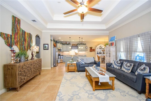 living room featuring ceiling fan, a raised ceiling, light tile patterned floors, arched walkways, and crown molding
