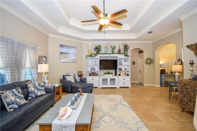 living room featuring arched walkways, crown molding, a ceiling fan, a tray ceiling, and light tile patterned flooring