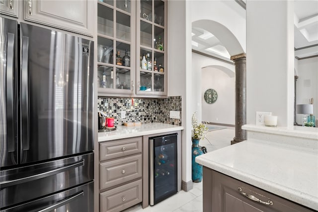 kitchen featuring decorative backsplash, decorative columns, stainless steel refrigerator, light stone countertops, and wine cooler