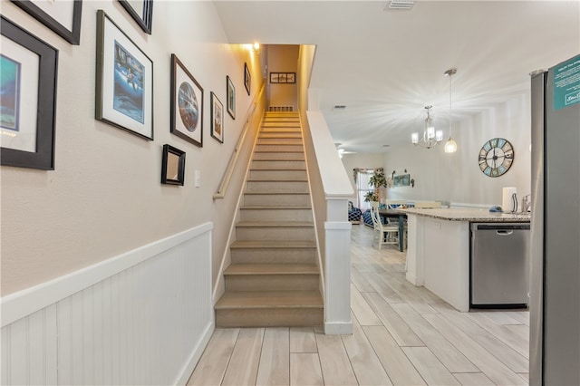 stairs with hardwood / wood-style floors and an inviting chandelier