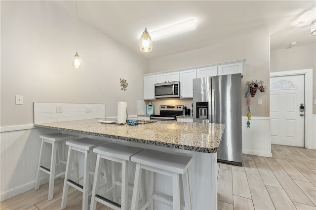 kitchen featuring white cabinetry, stainless steel appliances, kitchen peninsula, light hardwood / wood-style floors, and a breakfast bar