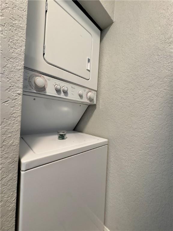 clothes washing area featuring laundry area, a textured wall, and stacked washing maching and dryer