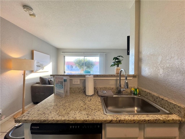 kitchen with dishwasher, a textured wall, a textured ceiling, a sink, and light tile patterned flooring