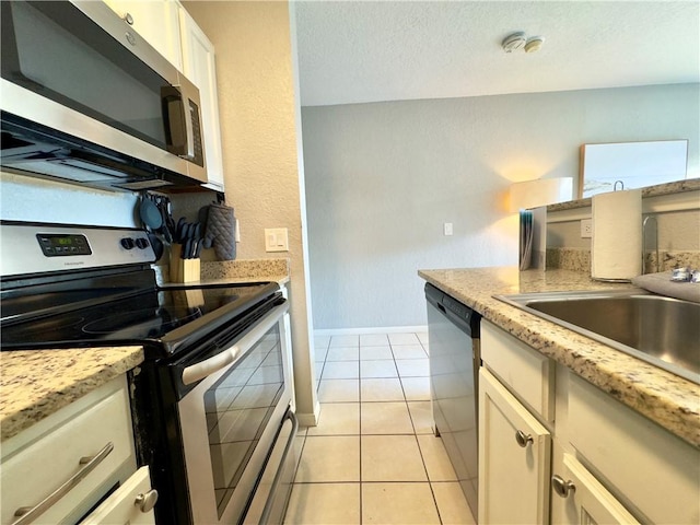 kitchen with light tile patterned floors, a sink, baseboards, appliances with stainless steel finishes, and light stone countertops