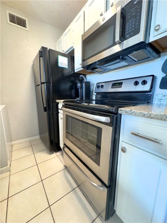 kitchen featuring visible vents, light stone counters, stainless steel appliances, white cabinetry, and light tile patterned flooring