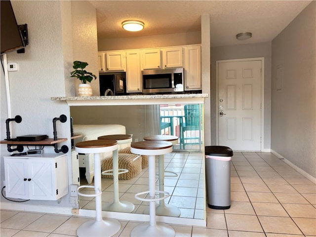 kitchen with black refrigerator, stainless steel microwave, baseboards, and light tile patterned floors