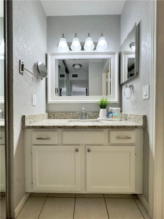 bathroom with a textured wall, tile patterned flooring, visible vents, and vanity