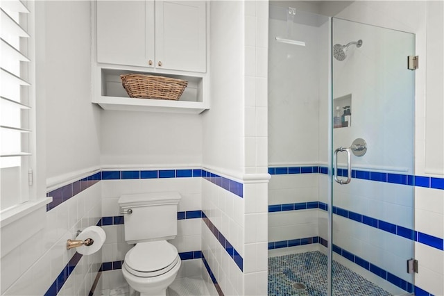 bathroom with wainscoting, a shower stall, toilet, and tile walls