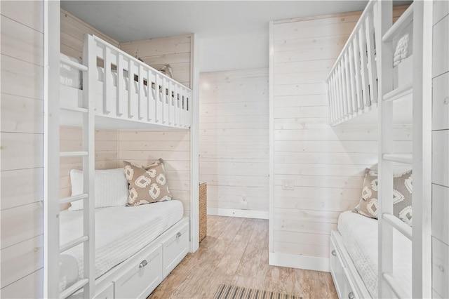 bedroom featuring baseboards, light wood-type flooring, and wooden walls