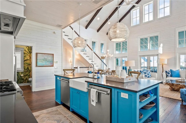 kitchen featuring dark countertops, open floor plan, blue cabinets, stainless steel dishwasher, and a sink