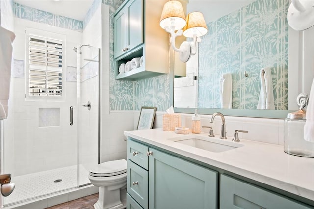 bathroom with vanity, a shower stall, toilet, and wallpapered walls