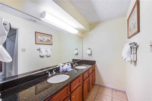 full bathroom featuring a textured ceiling, double vanity, tile patterned flooring, and baseboards