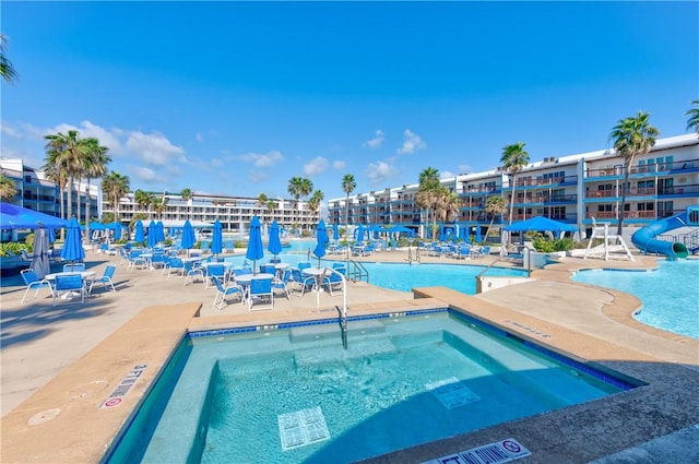 community pool featuring a water slide, a patio, and a hot tub