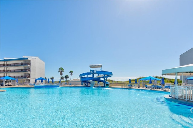 community pool with a water slide, fence, and a gazebo