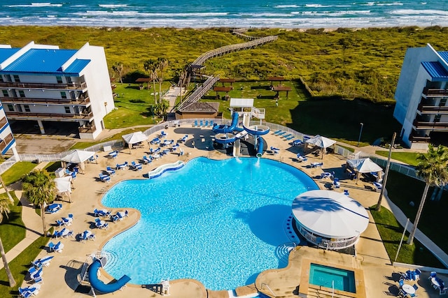 view of swimming pool featuring a patio, a water view, a beach view, and a water slide