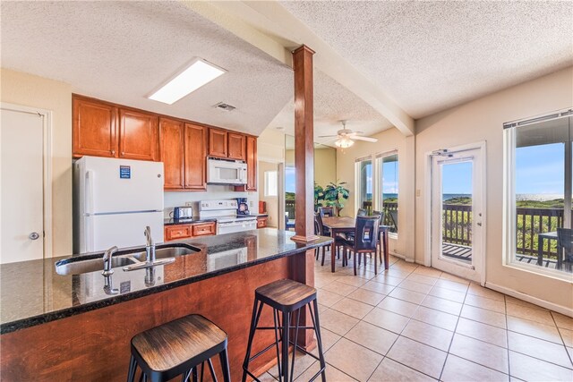 kitchen featuring a kitchen bar, dark stone countertops, beamed ceiling, white appliances, and ceiling fan