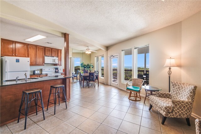 kitchen featuring kitchen peninsula, ceiling fan, a kitchen bar, light tile patterned floors, and white appliances