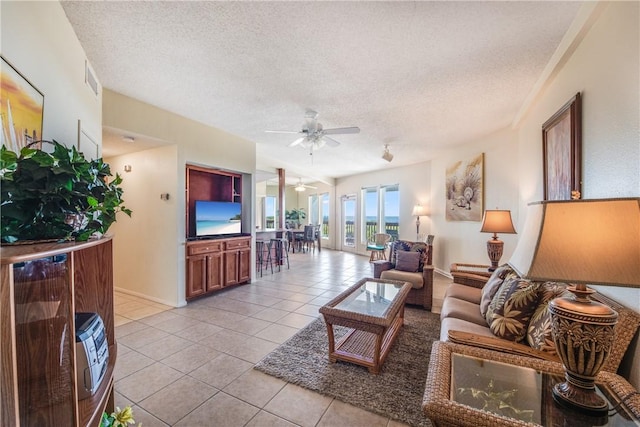 living room featuring a ceiling fan, a textured ceiling, light tile patterned flooring, and baseboards