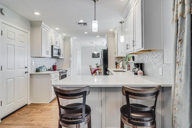 kitchen with kitchen peninsula, pendant lighting, stainless steel appliances, a breakfast bar, and white cabinets