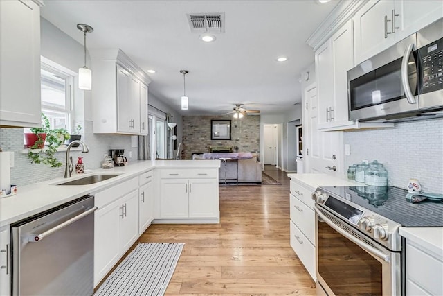 kitchen featuring kitchen peninsula, decorative light fixtures, white cabinets, appliances with stainless steel finishes, and sink