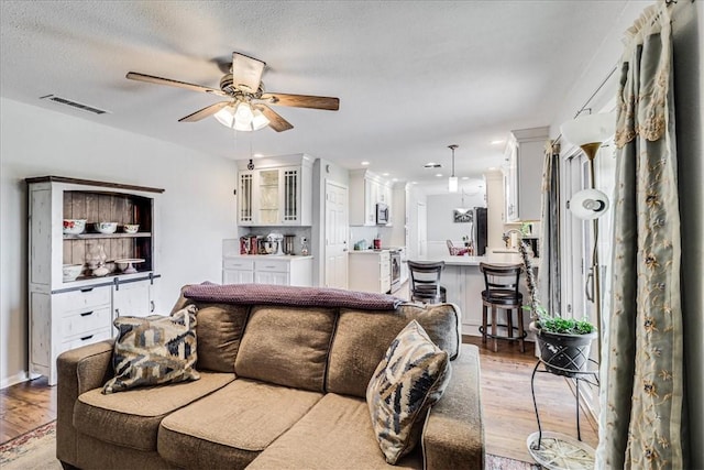 living room with a textured ceiling, ceiling fan, and light hardwood / wood-style flooring