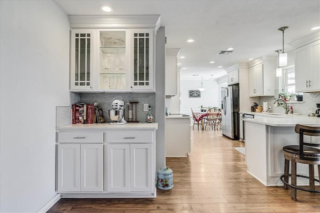 kitchen featuring pendant lighting, stainless steel refrigerator with ice dispenser, a kitchen bar, white cabinets, and sink