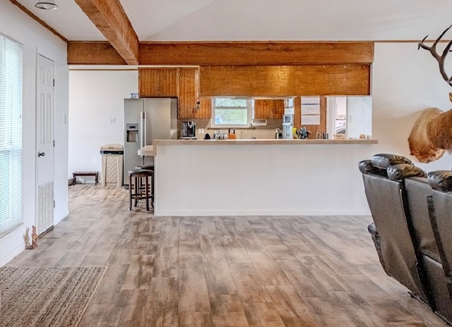 kitchen with light hardwood / wood-style floors, beamed ceiling, kitchen peninsula, a breakfast bar area, and stainless steel fridge