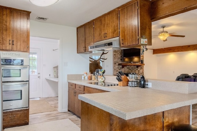 kitchen featuring light hardwood / wood-style floors, kitchen peninsula, ceiling fan, stainless steel double oven, and black electric stovetop