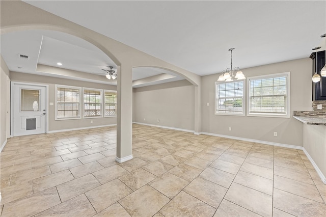 unfurnished dining area with ceiling fan with notable chandelier and a raised ceiling