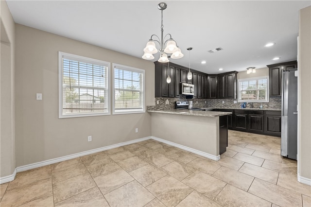 kitchen with appliances with stainless steel finishes, decorative light fixtures, decorative backsplash, sink, and kitchen peninsula