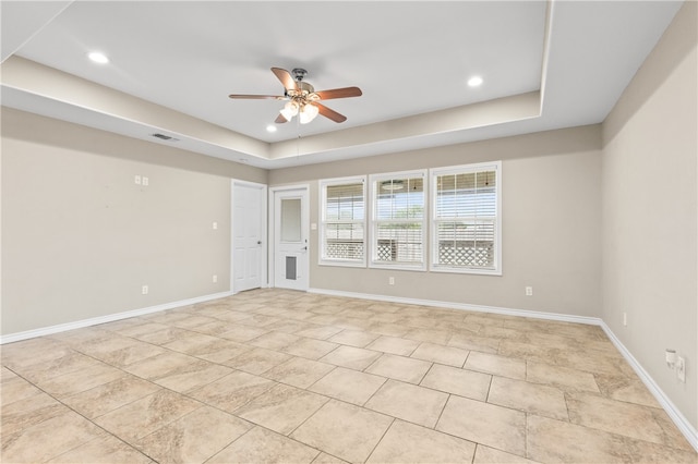 empty room with ceiling fan and a tray ceiling