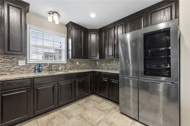 kitchen featuring light stone counters, stainless steel fridge, backsplash, dark brown cabinets, and sink