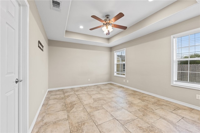 spare room featuring plenty of natural light, ceiling fan, and a tray ceiling