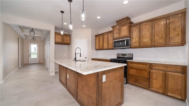 kitchen with appliances with stainless steel finishes, light stone counters, a kitchen island with sink, sink, and hanging light fixtures