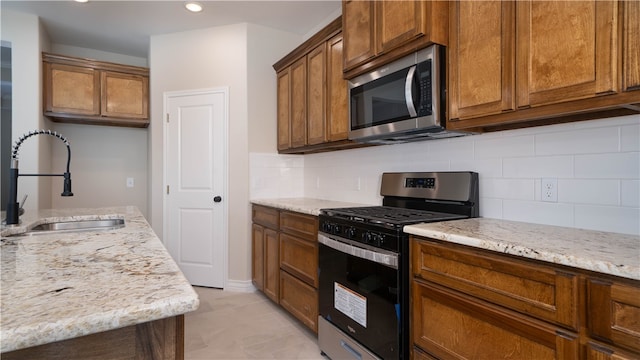 kitchen with light stone countertops, appliances with stainless steel finishes, tasteful backsplash, sink, and light tile patterned floors