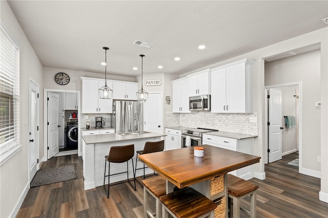 964 Allende St, Seguin, TX 78155 - kitchen with stainless steel appliances, washer / dryer, a sink, dark wood finished floors, and an island with sink