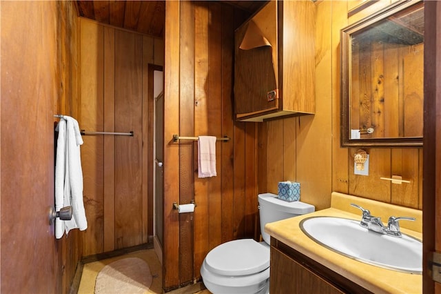 bathroom with vanity, toilet, and wood walls