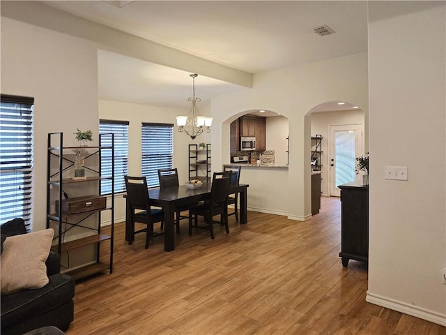 2421 Country Oaks Cir, Ingleside, TX 78362 - dining area with arched walkways, visible vents, baseboards, light wood-style floors, and an inviting chandelier