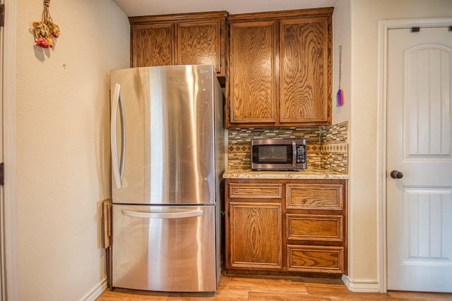 2421 Country Oaks Cir, Ingleside, TX 78362 - kitchen with baseboards, appliances with stainless steel finishes, light wood-type flooring, brown cabinets, and tasteful backsplash