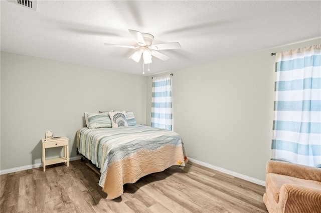 bedroom with a ceiling fan, visible vents, wood finished floors, and baseboards