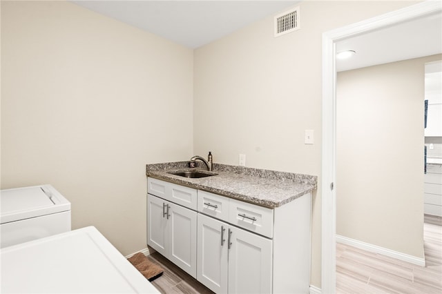 clothes washing area featuring light wood finished floors, visible vents, baseboards, and a sink