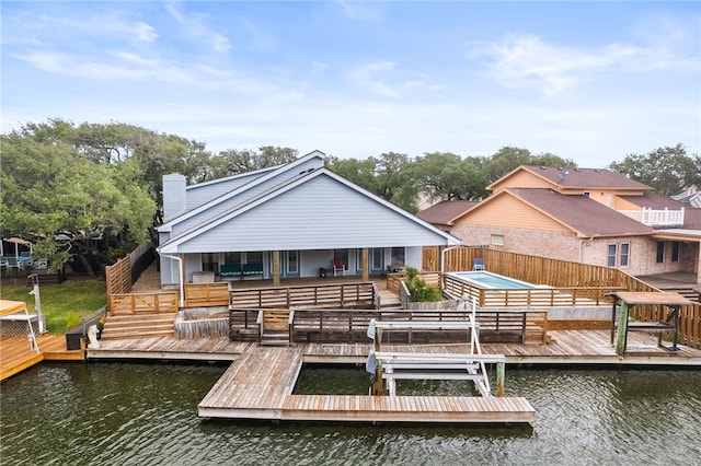 back of property with boat lift, fence, a water view, and a chimney