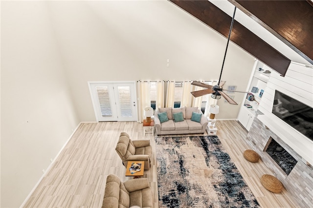 living area featuring a ceiling fan, baseboards, wood finished floors, a fireplace, and a high ceiling