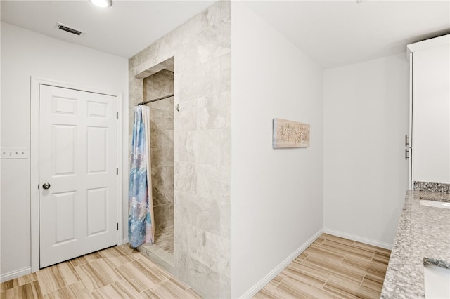 bathroom featuring a sink, visible vents, wood tiled floor, baseboards, and tiled shower