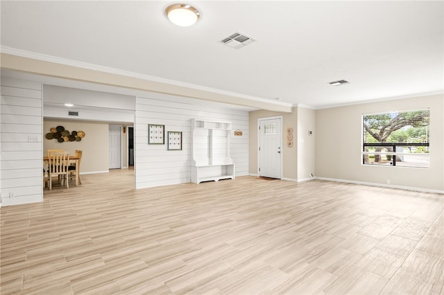 unfurnished living room featuring ornamental molding, visible vents, light wood finished floors, wooden walls, and baseboards