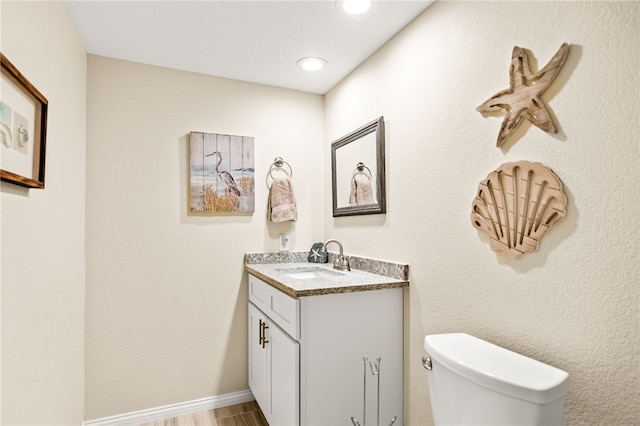 bathroom with vanity, toilet, wood finished floors, and recessed lighting