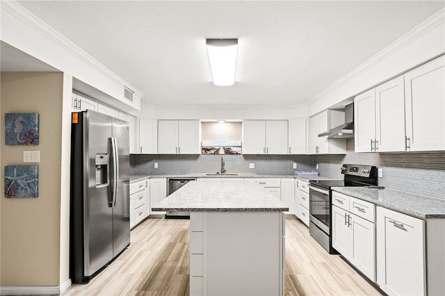 kitchen with a center island, a sink, wall chimney range hood, appliances with stainless steel finishes, and tasteful backsplash