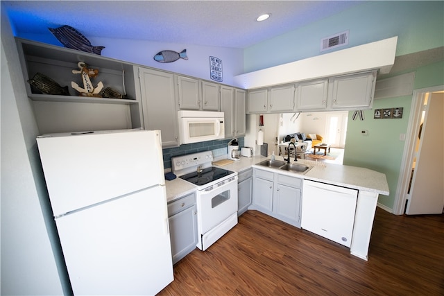 kitchen with dark hardwood / wood-style flooring, vaulted ceiling, kitchen peninsula, sink, and white appliances