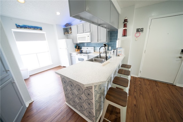 kitchen with dark wood-type flooring, kitchen peninsula, sink, a kitchen breakfast bar, and white appliances