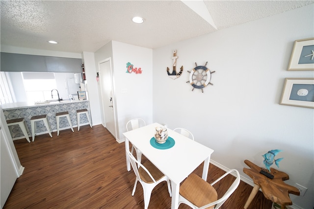 dining area featuring dark wood-type flooring, sink, and a textured ceiling